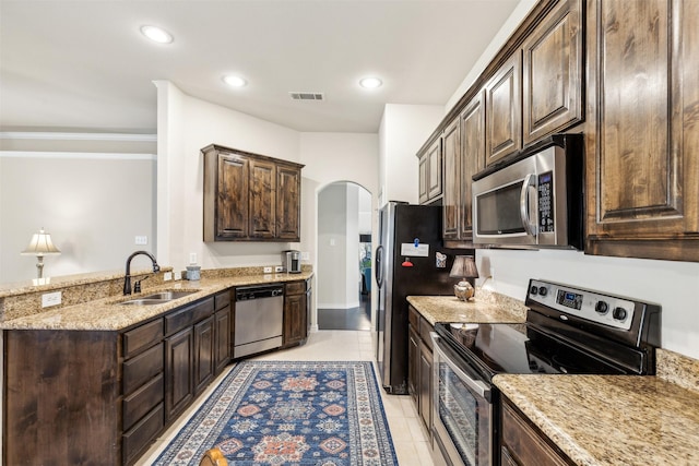 kitchen featuring light stone countertops, appliances with stainless steel finishes, dark brown cabinets, sink, and light tile patterned floors