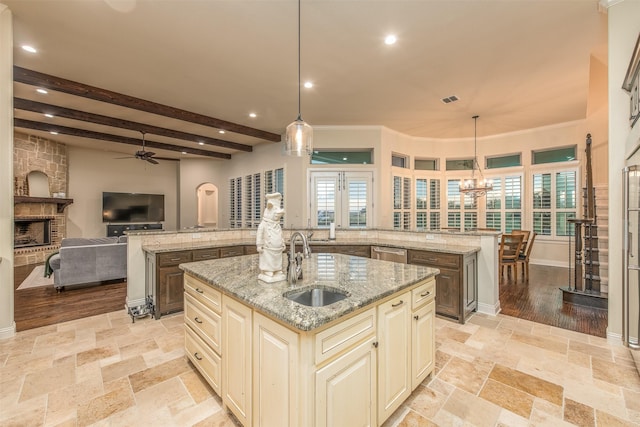 kitchen with light stone counters, a kitchen island with sink, hanging light fixtures, and cream cabinetry