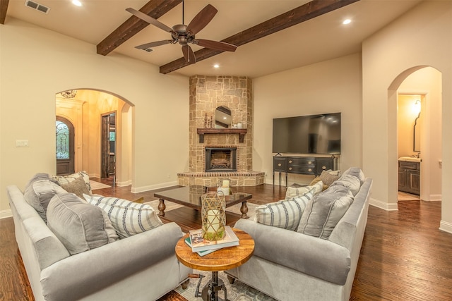 living room with ceiling fan, a stone fireplace, dark hardwood / wood-style floors, and beam ceiling