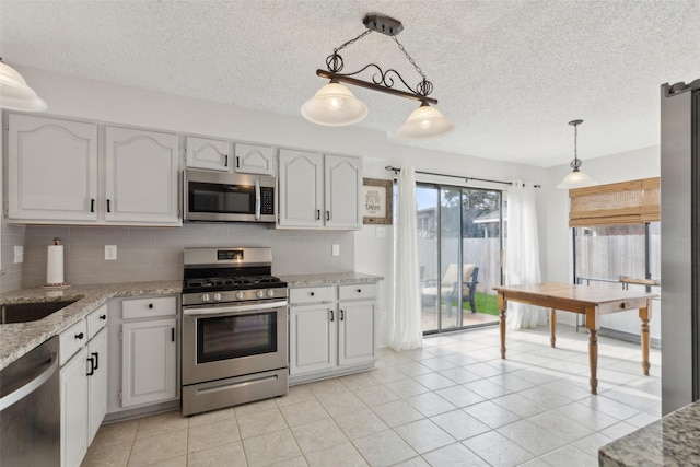 kitchen with white cabinets, hanging light fixtures, tasteful backsplash, light tile patterned flooring, and stainless steel appliances