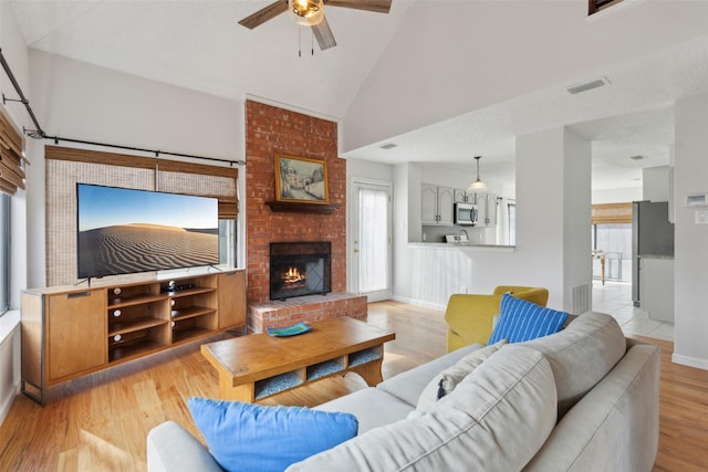 living room featuring a fireplace, light wood-type flooring, high vaulted ceiling, and ceiling fan