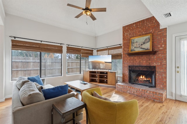 living room featuring a textured ceiling, light hardwood / wood-style flooring, a brick fireplace, and ceiling fan