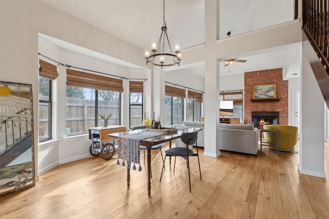 dining space featuring ceiling fan with notable chandelier, light wood-type flooring, a textured ceiling, a fireplace, and a towering ceiling