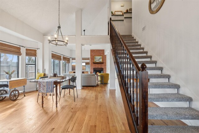 dining area featuring an inviting chandelier, wood-type flooring, a high ceiling, and a brick fireplace