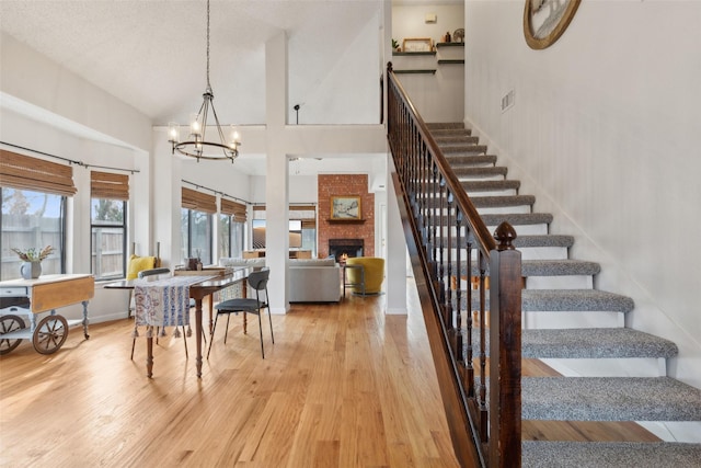 dining space with high vaulted ceiling, a fireplace, hardwood / wood-style floors, and a notable chandelier