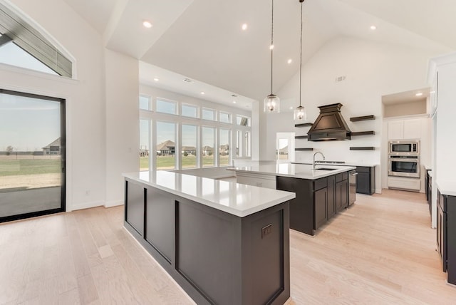 kitchen with high vaulted ceiling, an island with sink, decorative light fixtures, white cabinets, and appliances with stainless steel finishes