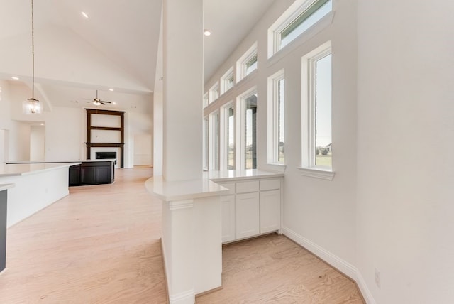 interior space featuring hanging light fixtures, white cabinetry, high vaulted ceiling, and light hardwood / wood-style flooring