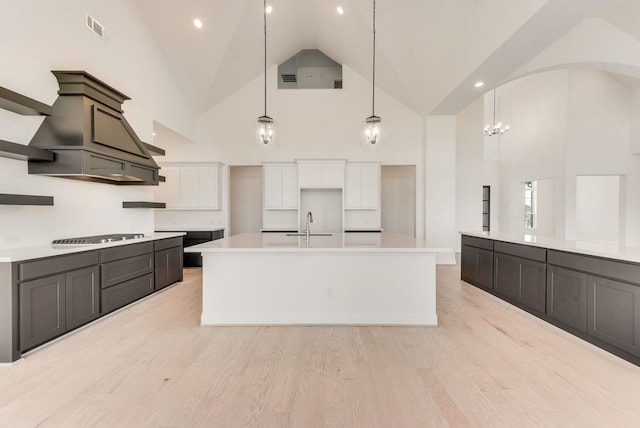 kitchen featuring high vaulted ceiling, decorative light fixtures, white cabinetry, and light hardwood / wood-style floors