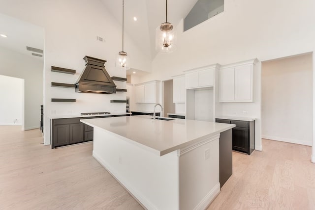 kitchen featuring premium range hood, gas stovetop, a kitchen island with sink, sink, and white cabinets