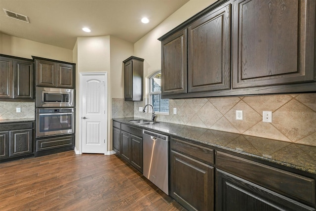 kitchen featuring dark wood-type flooring, sink, dark stone countertops, appliances with stainless steel finishes, and tasteful backsplash