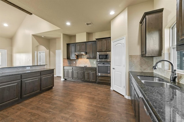 kitchen featuring appliances with stainless steel finishes, tasteful backsplash, dark brown cabinetry, dark wood-type flooring, and sink