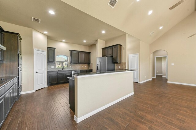 kitchen featuring a center island, dark wood-type flooring, stainless steel appliances, high vaulted ceiling, and decorative backsplash