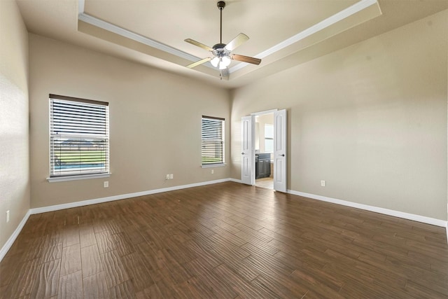 unfurnished bedroom featuring dark hardwood / wood-style floors, a raised ceiling, multiple windows, and ceiling fan