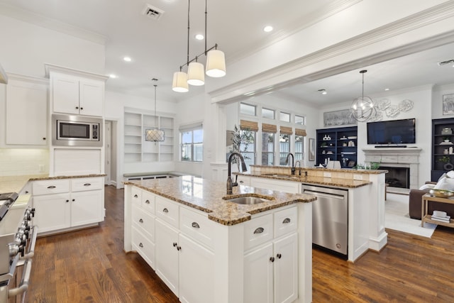 kitchen featuring appliances with stainless steel finishes, light stone counters, sink, pendant lighting, and a center island with sink