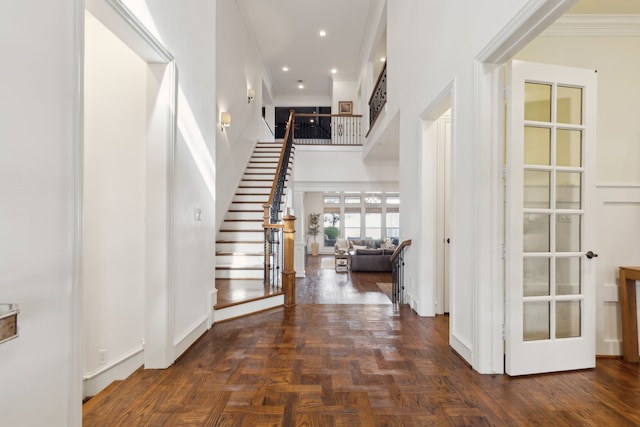 foyer entrance featuring dark parquet flooring, a towering ceiling, french doors, and ornamental molding