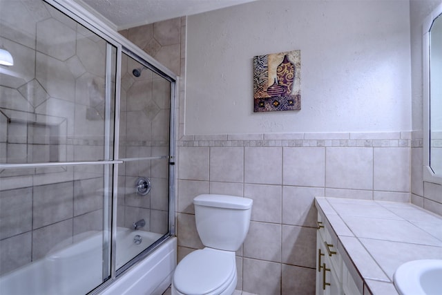 full bathroom with vanity, combined bath / shower with glass door, tile walls, and toilet