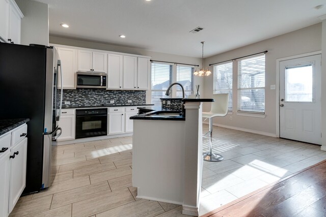 kitchen featuring sink, stainless steel appliances, decorative light fixtures, a center island with sink, and white cabinets