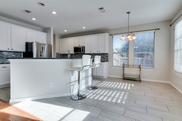 kitchen with white cabinetry, hanging light fixtures, stainless steel appliances, an inviting chandelier, and an island with sink