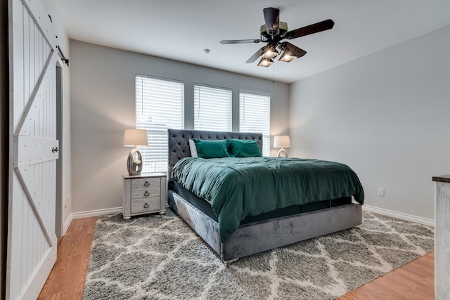 bedroom featuring a barn door, hardwood / wood-style flooring, and ceiling fan