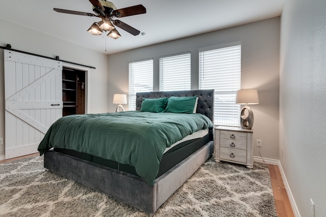 bedroom with a barn door, ceiling fan, and hardwood / wood-style flooring