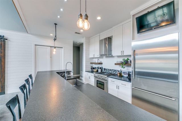 kitchen with pendant lighting, high quality appliances, wall chimney range hood, and white cabinets