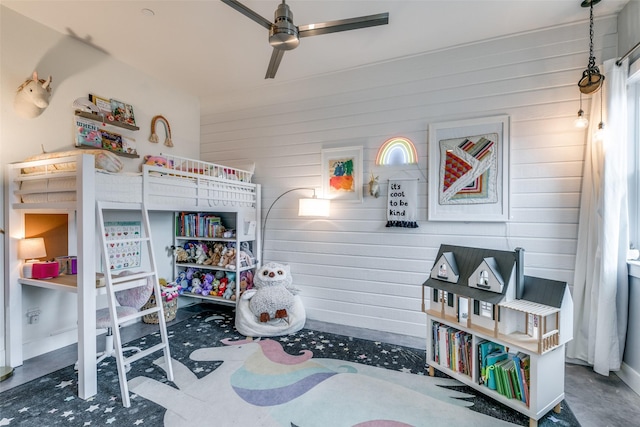 bedroom with ceiling fan, wood walls, and concrete floors