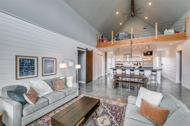 living room with a barn door, ceiling fan, wooden walls, and high vaulted ceiling