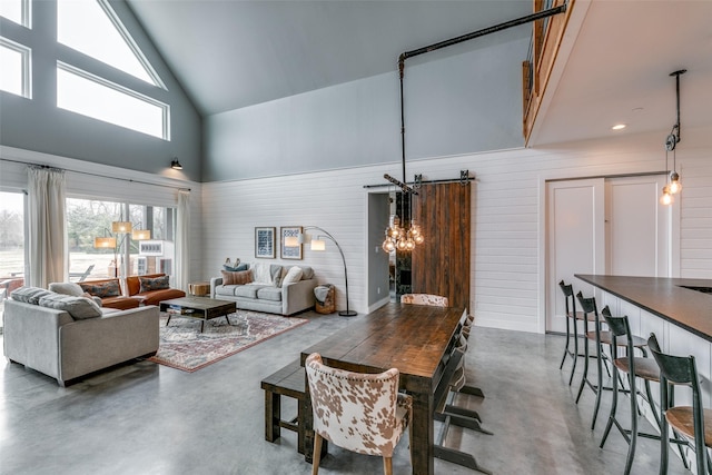 living room featuring wood walls, concrete floors, a high ceiling, and a notable chandelier