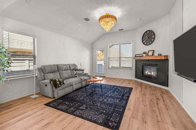 living room with a notable chandelier, vaulted ceiling, and light hardwood / wood-style flooring