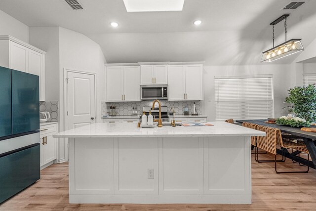 kitchen featuring light stone counters, a center island with sink, white cabinets, and stainless steel appliances