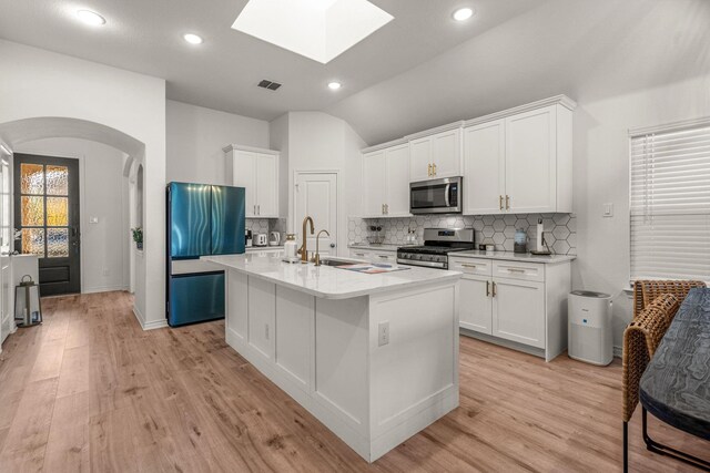 kitchen featuring white cabinets, lofted ceiling with skylight, a kitchen island with sink, and appliances with stainless steel finishes