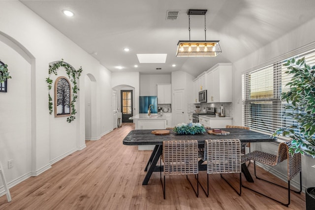 dining space with a skylight, sink, and light wood-type flooring