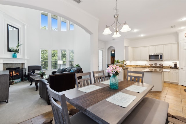 dining room with light tile patterned flooring, sink, a tiled fireplace, a high ceiling, and an inviting chandelier