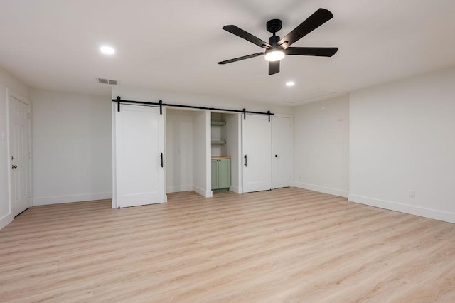 unfurnished bedroom with light wood-type flooring, a barn door, and ceiling fan