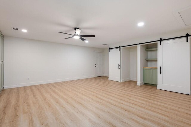 unfurnished bedroom featuring ceiling fan, a barn door, and light wood-type flooring