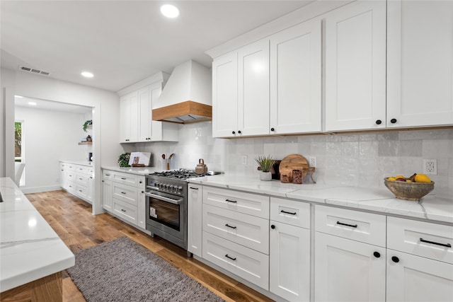 kitchen with white cabinetry, premium range hood, high end stove, light hardwood / wood-style floors, and decorative backsplash