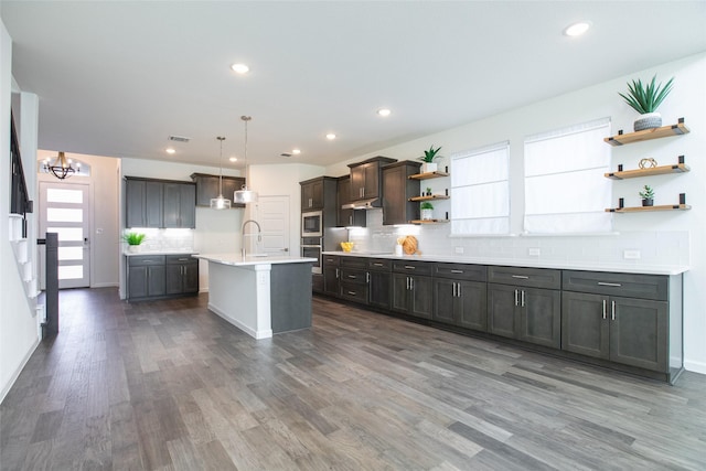 kitchen featuring dark wood-type flooring, a center island with sink, sink, decorative light fixtures, and dark brown cabinets