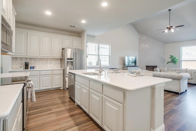 kitchen with sink, a large fireplace, an island with sink, stainless steel appliances, and white cabinets