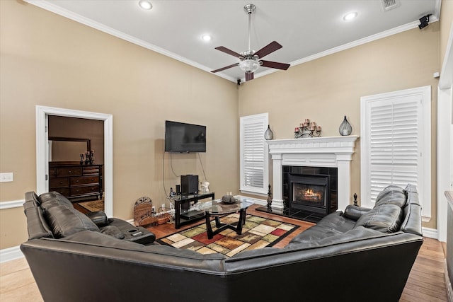 living room with hardwood / wood-style floors, ceiling fan, crown molding, and a tiled fireplace