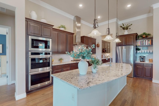 kitchen featuring light stone countertops, hanging light fixtures, wall chimney range hood, a kitchen island with sink, and appliances with stainless steel finishes