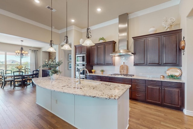 kitchen featuring dark brown cabinetry, sink, stainless steel appliances, wall chimney range hood, and decorative light fixtures