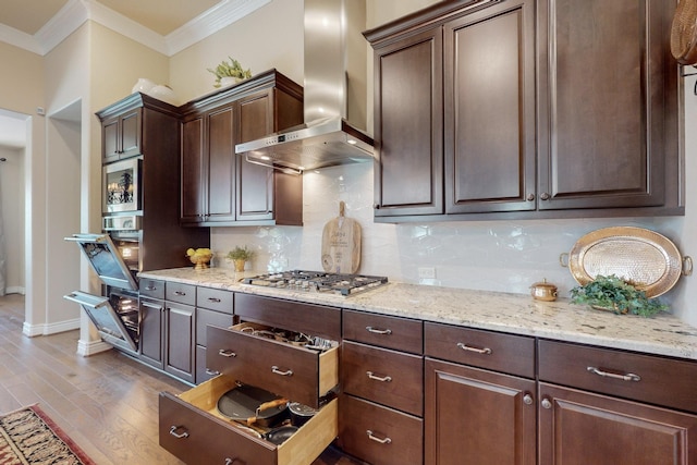 kitchen featuring dark brown cabinetry, wall chimney range hood, stainless steel appliances, and light wood-type flooring