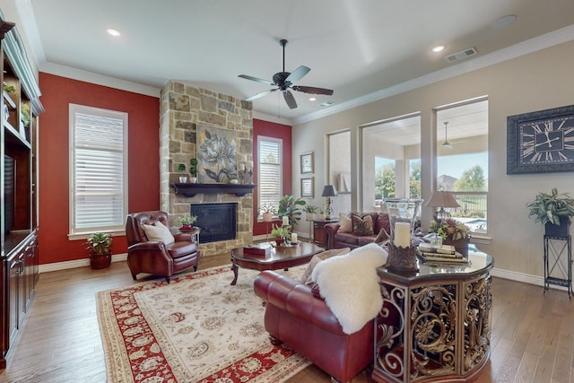 living room with a stone fireplace, ceiling fan, light hardwood / wood-style flooring, and crown molding