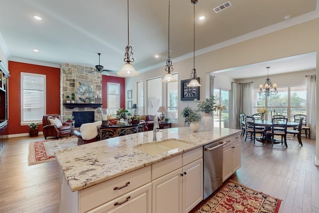 kitchen featuring a fireplace, sink, a center island with sink, dishwasher, and hanging light fixtures