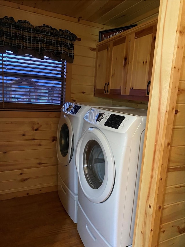 clothes washing area with cabinet space, wooden walls, wood finished floors, and washing machine and clothes dryer