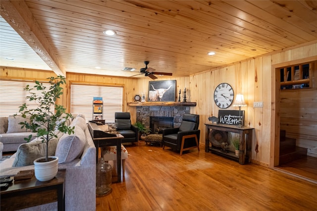 living room with a stone fireplace, wood walls, wooden ceiling, and wood finished floors