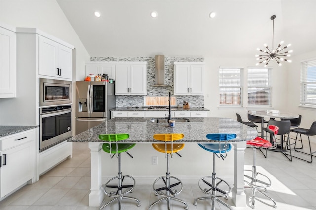 kitchen featuring vaulted ceiling, a kitchen island with sink, stainless steel appliances, and wall chimney range hood