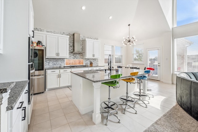 kitchen featuring white cabinetry, sink, decorative light fixtures, and wall chimney range hood