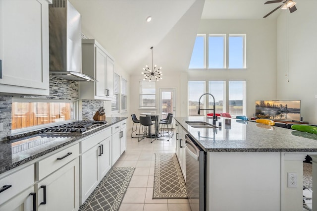 kitchen featuring wall chimney exhaust hood, stainless steel appliances, sink, dark stone countertops, and an island with sink