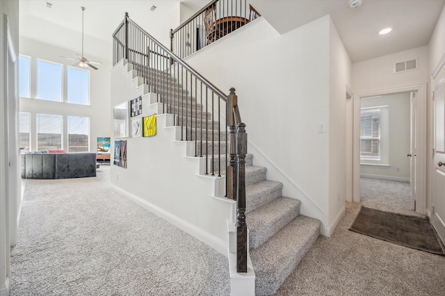 stairway with a high ceiling, carpet floors, and ceiling fan